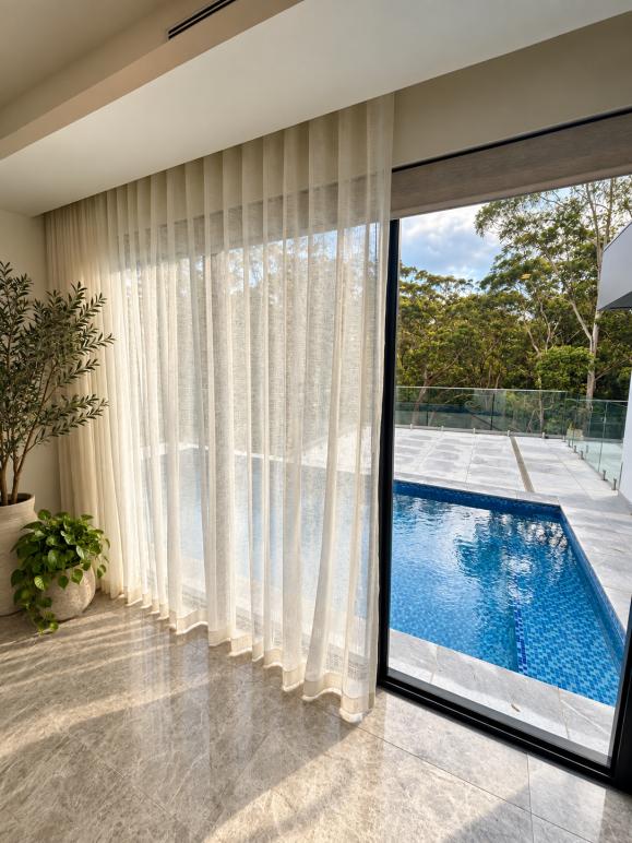 Full-height sheer curtains beside a sliding door opening onto a pool