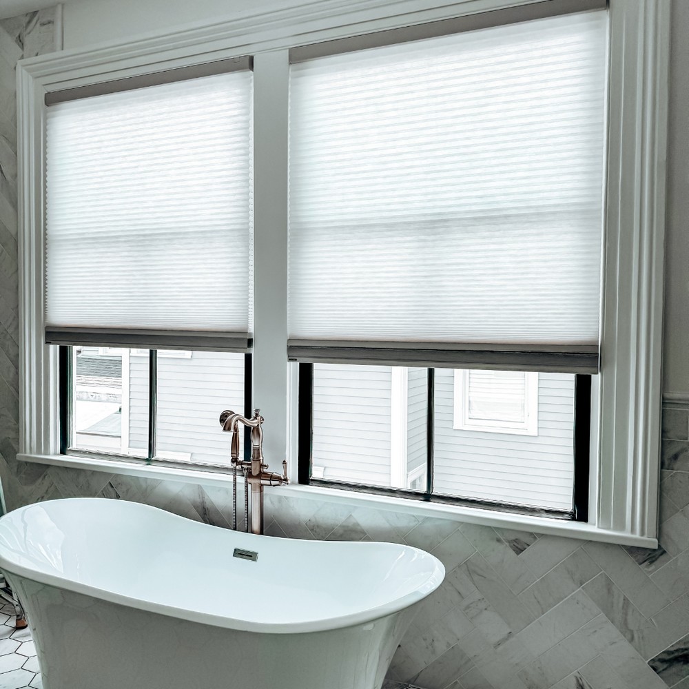 White honeycomb blinds filtering light above a freestanding bath