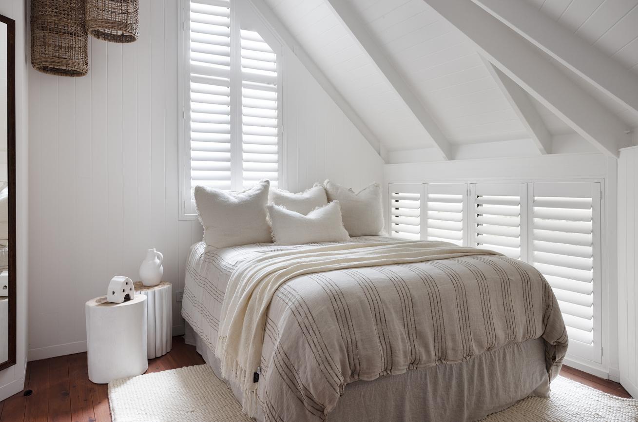 White plantation shutters in a bedroom with a raked timber ceiling